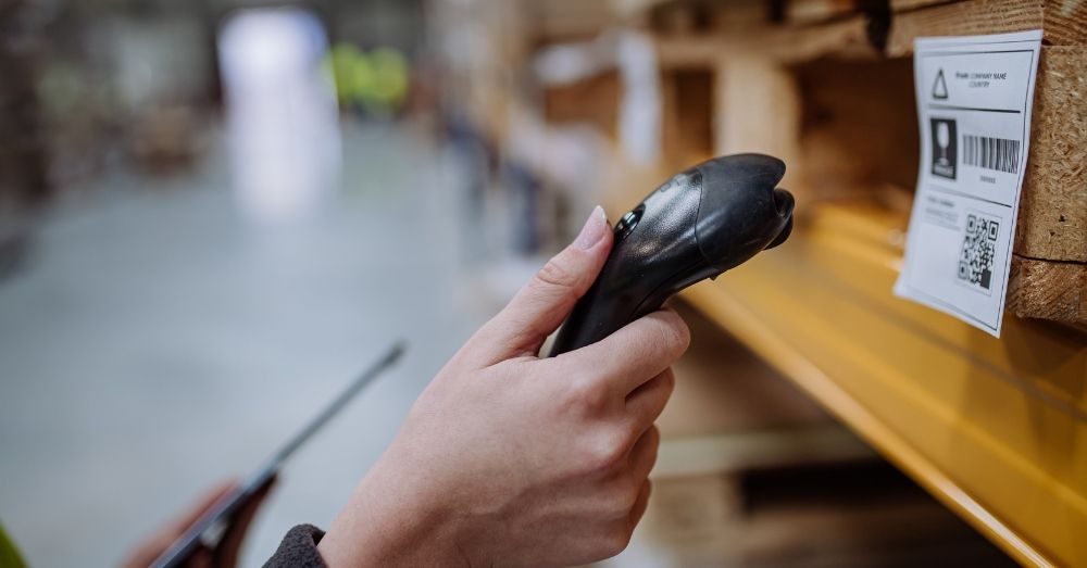 Worker using a handheld barcode scanner to scan a label on a warehouse shelf.