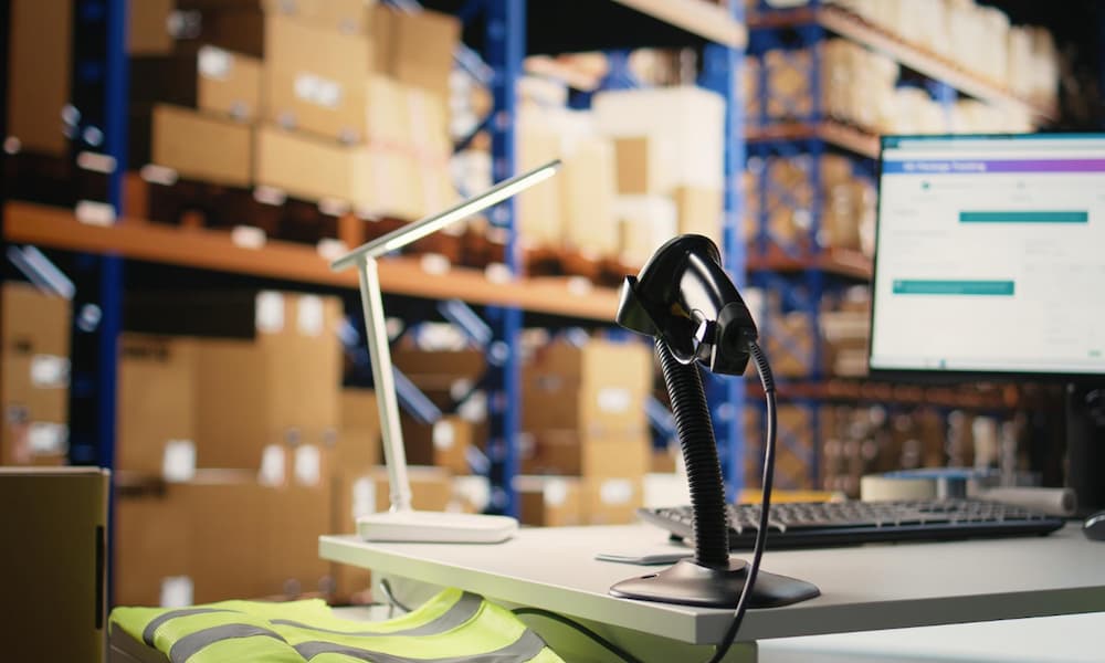 Warehouse workstation with barcode scanner, computer, and inventory shelves in the background