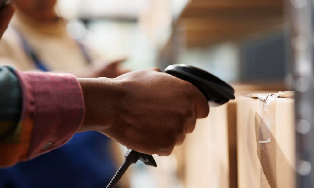 Worker scanning box with RFID barcode scanner in warehouse.