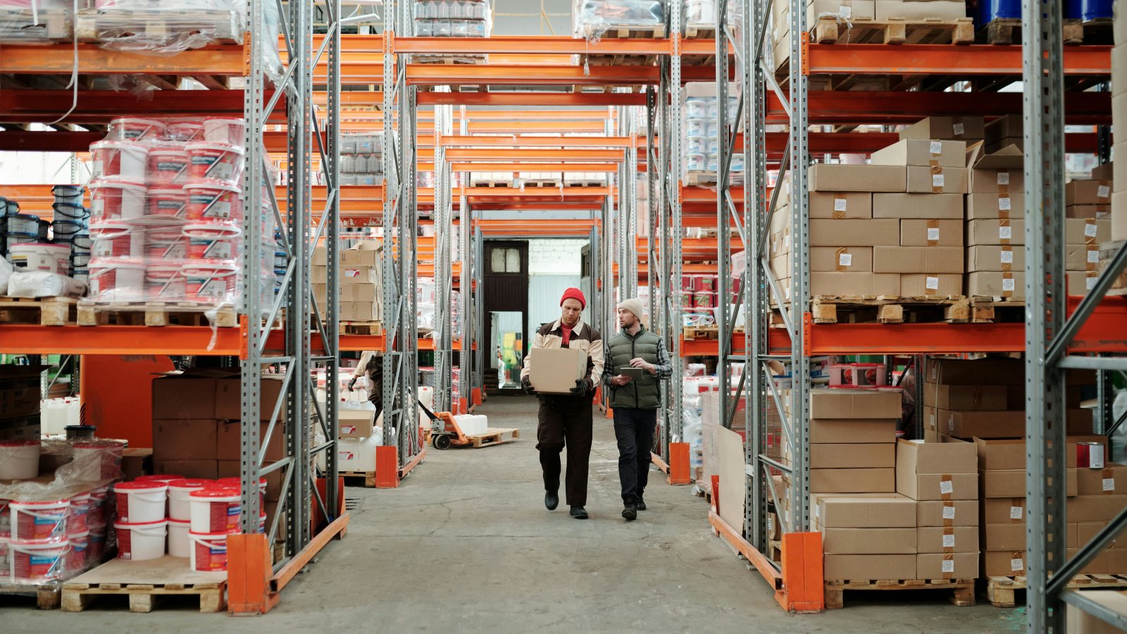 Two workers handling a package in a spacious warehouse with shelves stocked with boxes and products